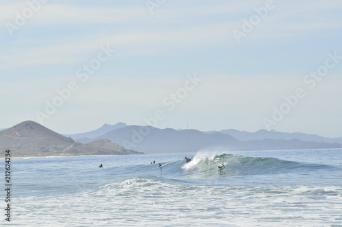 surfers riding ocean wave in Baja hills and mountains coastal landcape