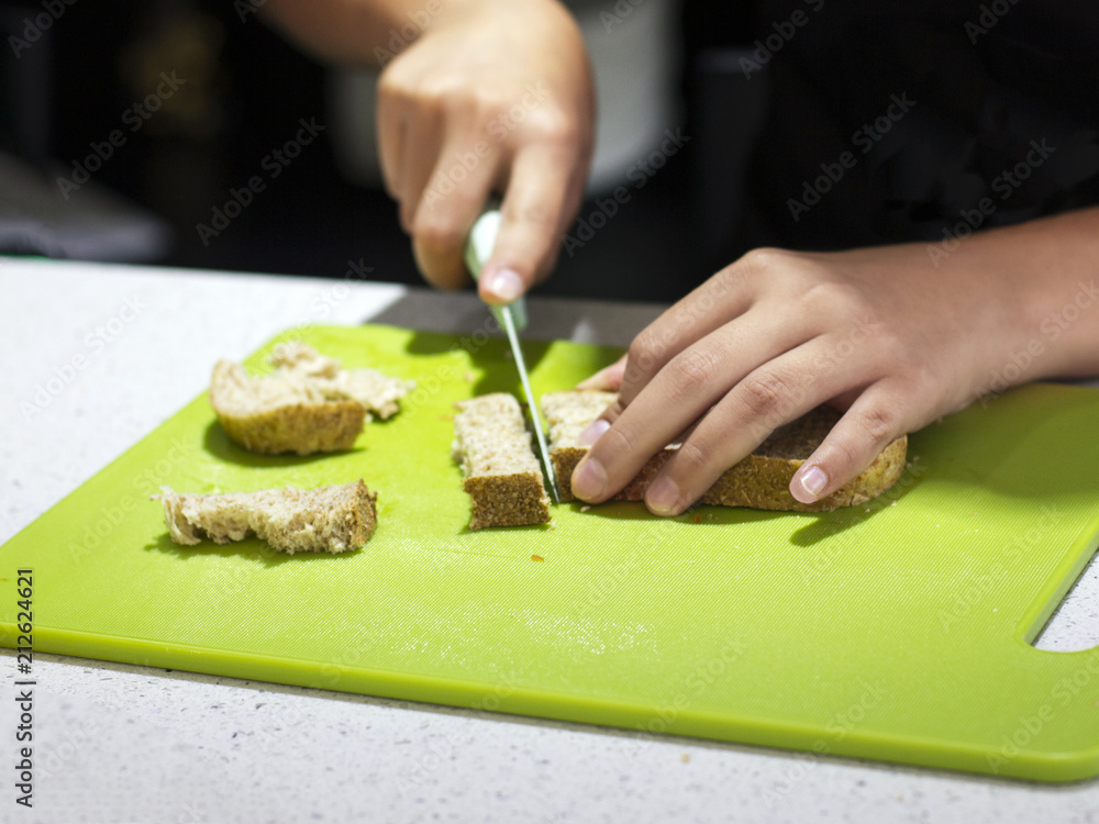 Hands of the cook cut bread with a knife on a green board