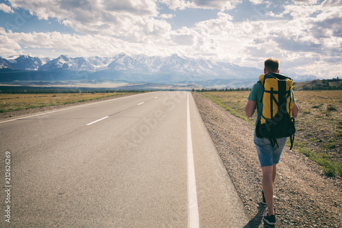 Man walks along an asphalt road with a backpack on his back overlooking the mountains