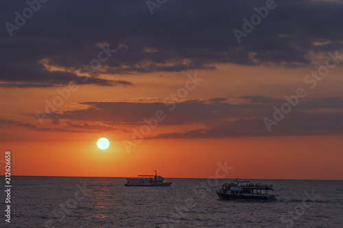 Beautiful seascape with boat in the sea at sunset with a colorful evening sky and a round disk of sun over the sea. © dzmitrock87