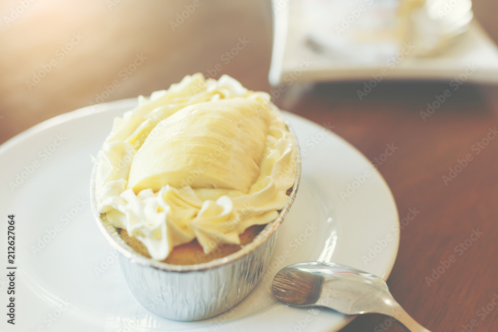 A piece of Durian cake put on the white dish with a silver spoon for serving to sweet lover people. A piece of Durian cake put on the white dish with a silver spoon for serving to sweet lover people.