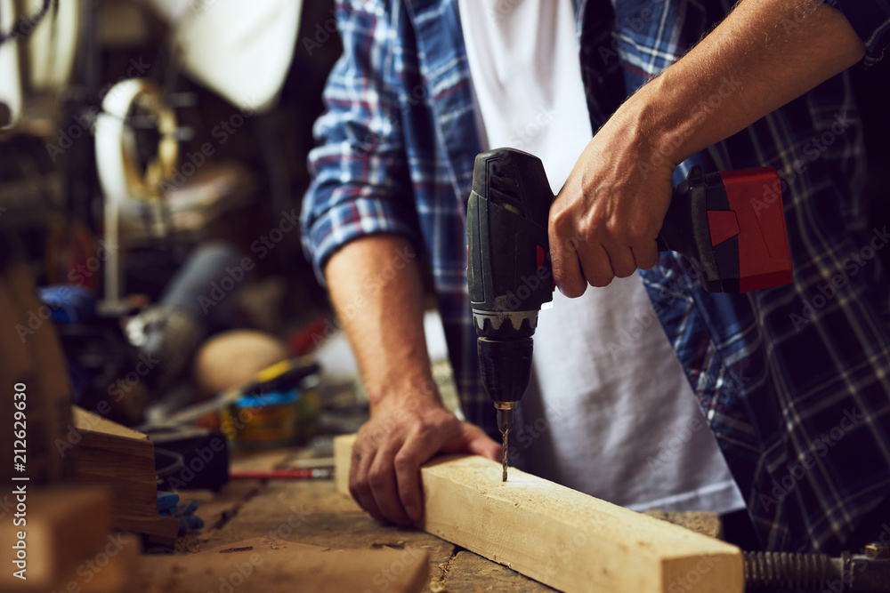 Carpenter working in his workshop with an electric drill into a wooden board Carpenter working in his workshop with an electric drill into a wooden board