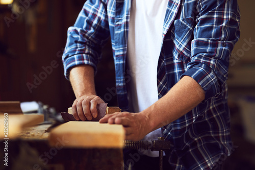 Carpenter works with sandpaper on a wooden plank in a carpentry shop photo
