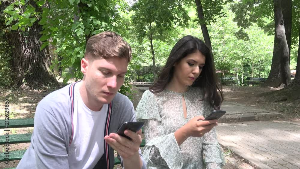 Modern contemporary friends sitting on park bench sending online phone messages Modern contemporary friends sitting on park bench sending online phone messages