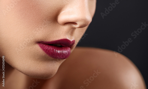 Cropped close up of woman's plump lips covered with dark lipstick. Pretty young face with beatiful heatures, smooth and healthy skin, little nose. Posing on black studio background.