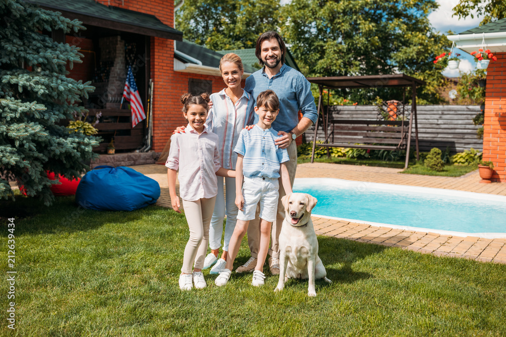 Fototapeta premium cheerful family with labrador dog looking at camera while standing on backyard of country house on summer day