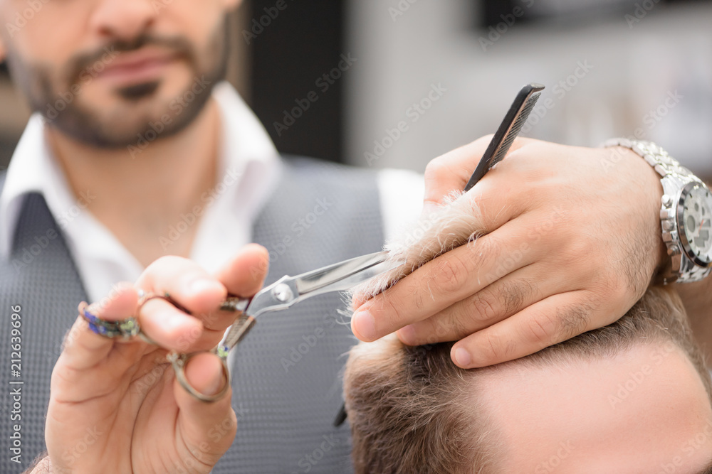 Photo of barber working with client in barbershop. Making professional haircut. Hairstyle looking fashionable, stylish. Hairdresser holding sharp scissors and plastic comb, wearing shirt, waistcoat. Photo of barber working with client in barbershop. Making professional haircut. Hairstyle looking fashionable, stylish. Hairdresser holding sharp scissors and plastic comb, wearing shirt, waistcoat.