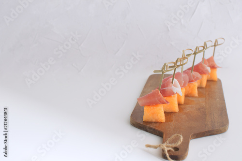 Melon with prociutto canapes on skewers Melong with jamon on wooden chopping board Restaurant gourmet dish Traditional italian Spanish appetizer tapas White background copy space photo