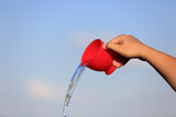 Kobieca dłoń wylewa wodę z czerwonej filiżanki.