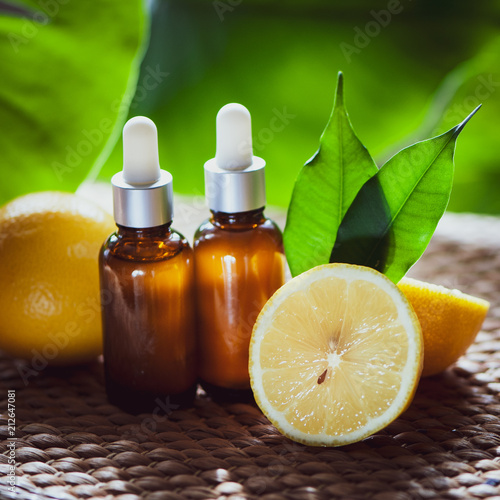 Bottles with lemon oil, fresh fruit whole and half on a natural tropical background.