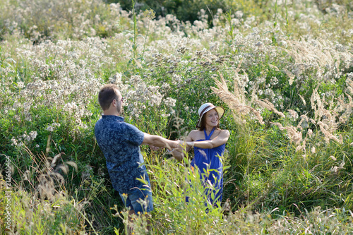 Young couple in love playing in the meadow of flowers at sunset and holding hands. Landscape orientation