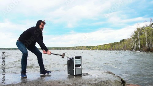 Concept of freedom from computer addiction - Man breaks system unit of a computer with a hummer outside, lake with forest background. Angry man destroying a laptop or computer with a hammer. photo