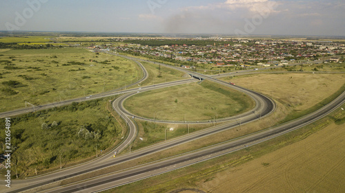 Summer aerial drone photo of transport junction, traffic cross road junction day view from above with green tree circle road, near is a wheat field. Top down view of traffic jam.