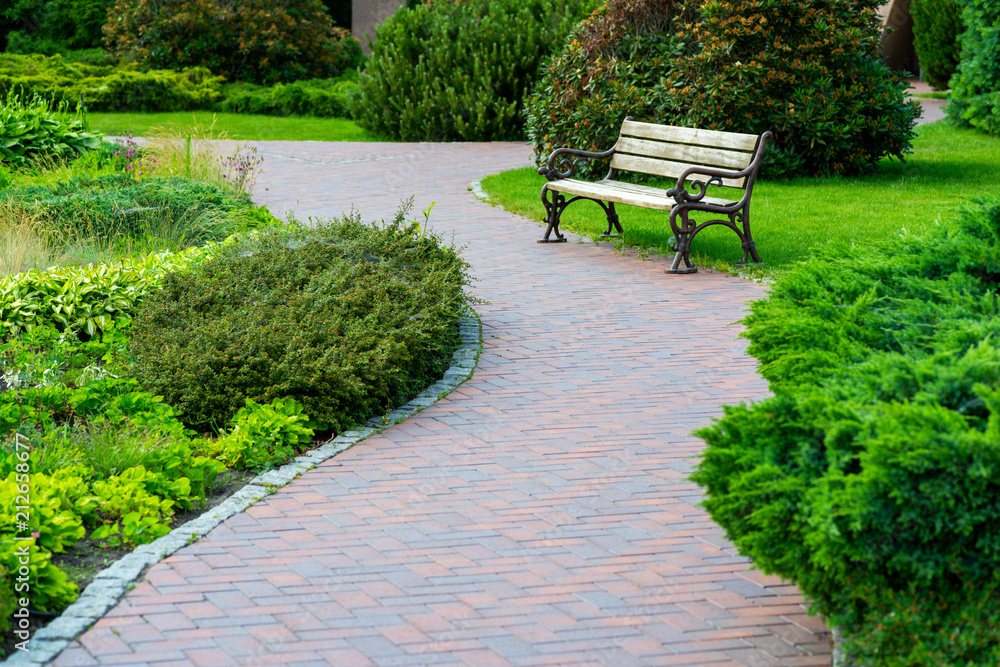 A stone tile path with a wooden seat in a green park with a landscape design A stone tile path with a wooden seat in a green park with a landscape design