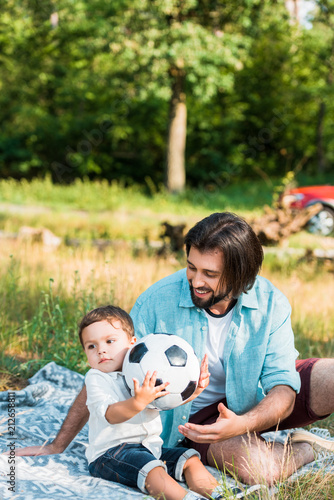 happy father and toddler son playing with football ball at picnic