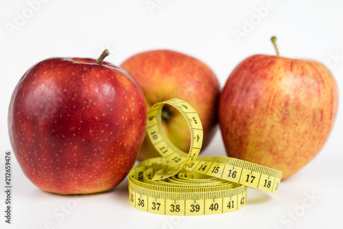 Red apples and a measure of tailor on a white table. Ripe fruits and a tailor's centimeter.