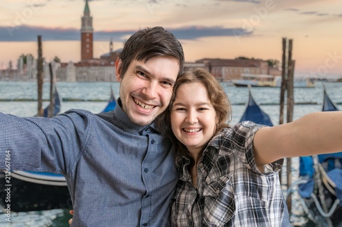 Young couple is taking selfie photo in Venice in Italy. Venetian gondolas in background.