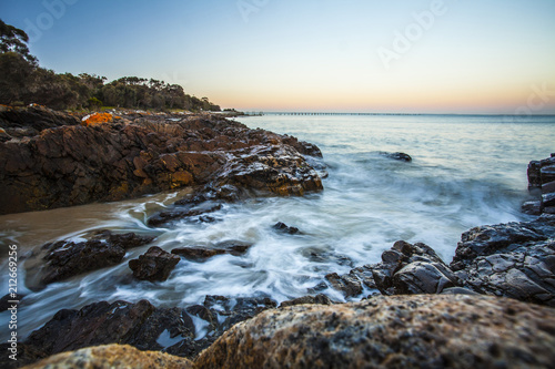 Moving waves breaking over rocky shore at sunrise