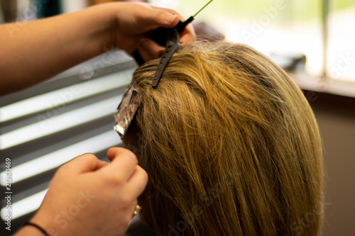 Blonde woman receiving haircut at a salon. Woman with blonde highlights. Hair foils on a female client. Master stylist cutting hair