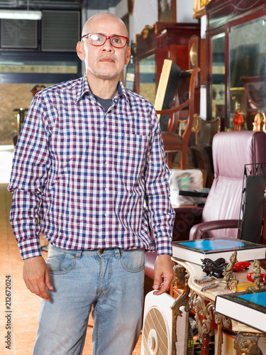 Portrait of successful owner of antiques shop among vintage things