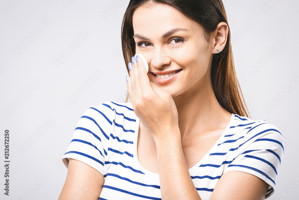 A picture of a happy woman cleaning her face with cotton pads over white background