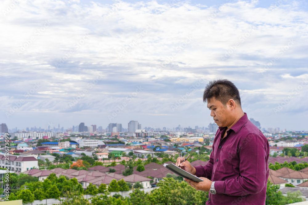 young man writing notes standing in a city view background