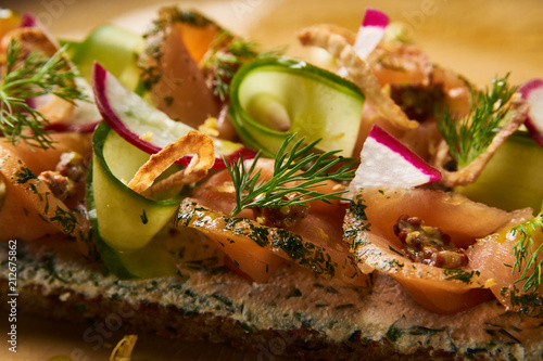 Smorrebrod Danish sandwich with salmon fish, curd mousse, marinated cucumber and radish. Delicious vegetarian snack food with dark rye bread and different topping on plate at restaurant table top view