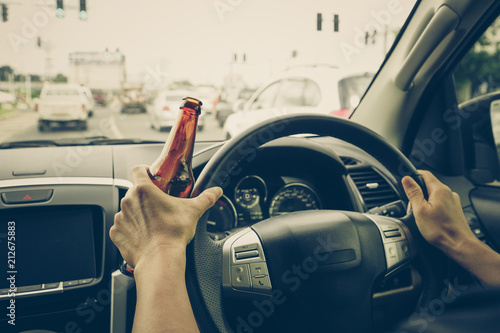 A driver holding alcoholic bottle while driving / Drunk driving concept