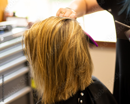 Professional master hair stylist blow drying a female client's blonde hair. Highlights in hair of female client at a salon