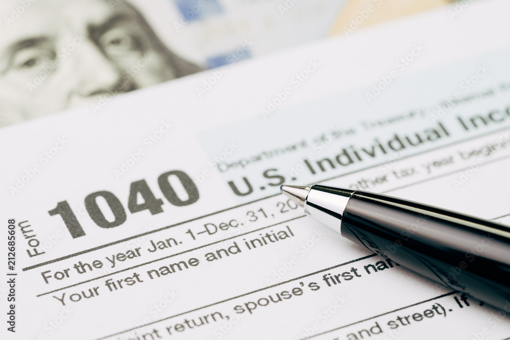 Tax time concept, selective focus on pen on 1040 US individual income tax filling form with US dollar bill, calculate from yearly revenue to pay the government Tax time concept, selective focus on pen on 1040 US individual income tax filling form with US dollar bill, calculate from yearly revenue to pay the government