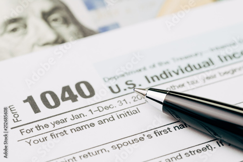 Tax time concept, selective focus on pen on 1040 US individual income tax filling form with US dollar bill, calculate from yearly revenue to pay the government