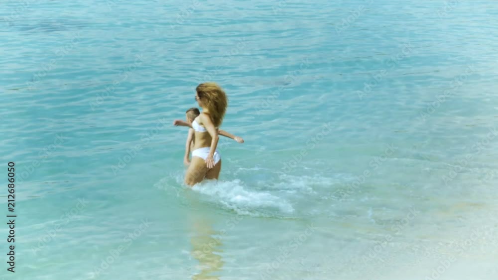 Mother playing with her little son and running in the sea at tropical beach Mother playing with her little son and running in the sea at tropical beach
