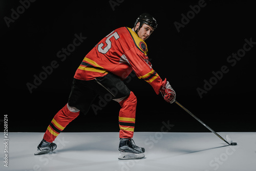 young professional sportsman playing ice hockey on black