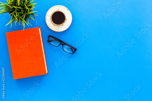 Intellectual entertainment concept. Books with empty cover near glasses, coffe, plant on blue desk top view copy space