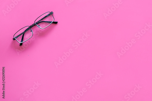 One glasses with transparent lenses on pink background top view copy space