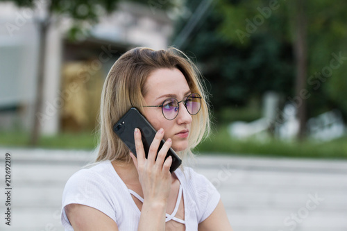 Portrait of young woman in eyeglasses talking on the phone outdoors