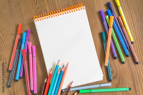 bright multicolored pencils and markers next to a sketchbook on a wooden table