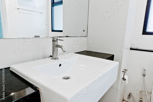 Close-up small basin and mirror in small bathroom, on white ceramic wall.