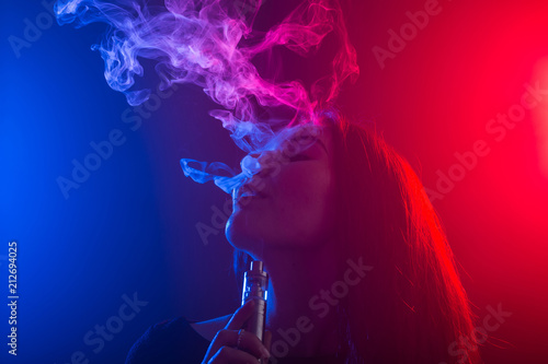 Close up portrait of vaping girl in neon blue and red light.