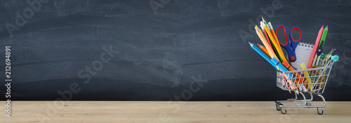 Banner of Shopping cart with school supply in front of blackboard. Back to school concept. photo