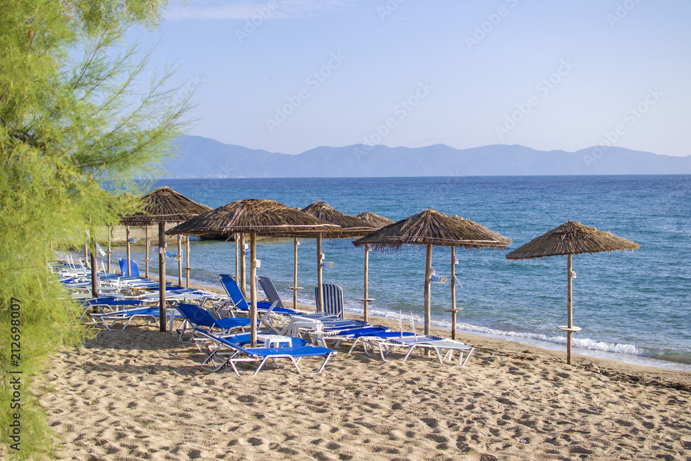 Ierissos beach with loungers under palm tree leaves umbrellas