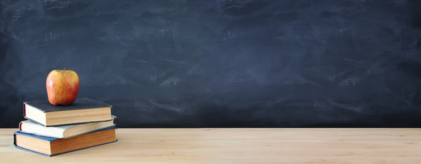 back to school concept. stack of books and apple over wooden desk in front of blackboard.