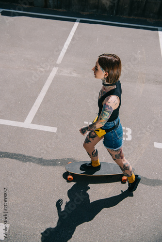 overhead view of stylish tattooed girl skateboarding at parking lot