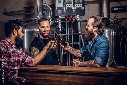 Three bearded interracial friends drink craft beer in a brewery.