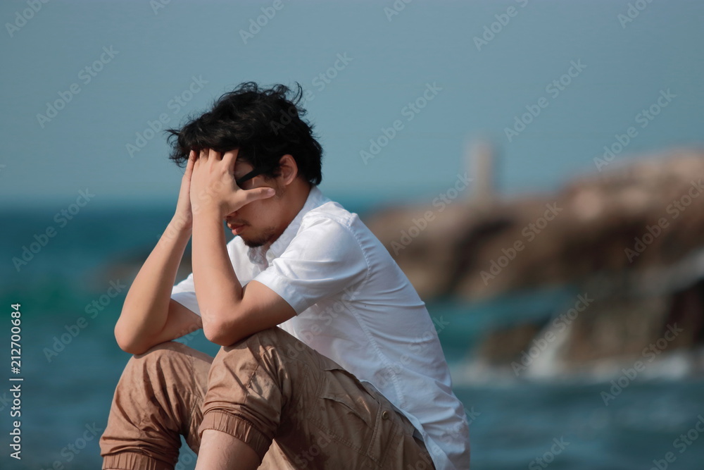Anxious depressed Asian man covering face with hands and bend down head
