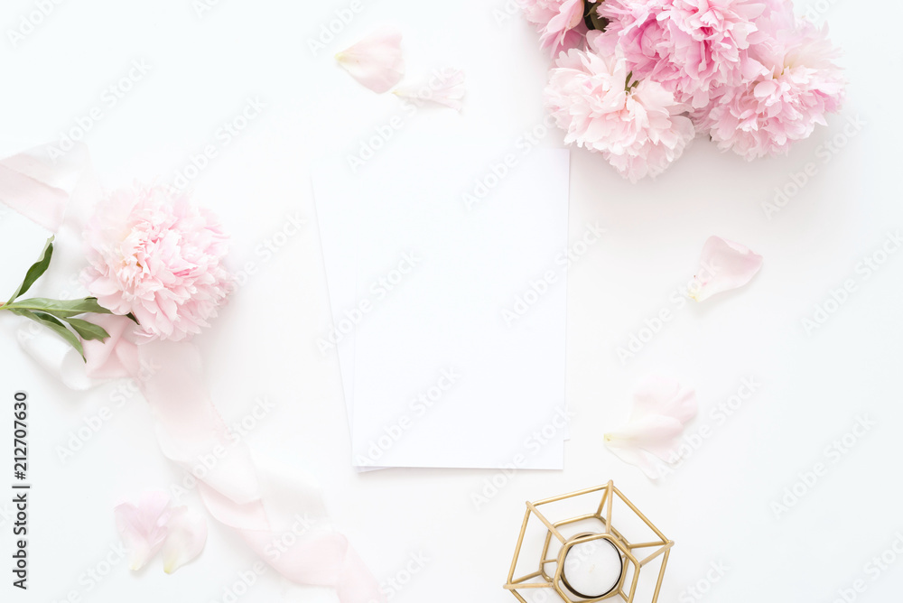Styled feminine top view.on white background with wedding card, pink peonies petals, candle