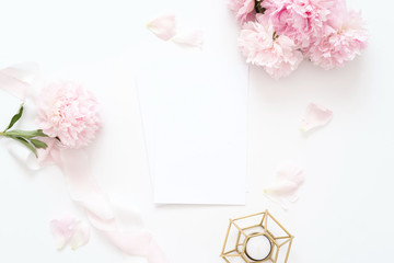 Styled feminine top view.on white background with wedding card, pink peonies petals, candle