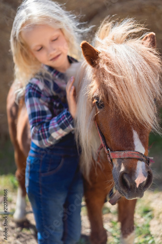 kid touching cute pony fur at farm