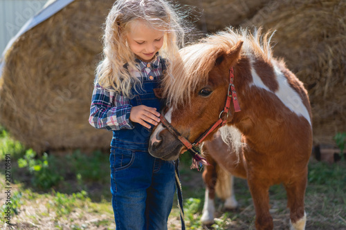 Canvas Print happy kid palming cute pony at farm