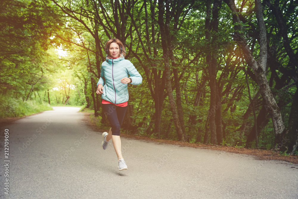 A young blonde woman running is practicing outdoors in a city mountain park in the forest. Warm rays through the branches of trees A young blonde woman running is practicing outdoors in a city mountain park in the forest. Warm rays through the branches of trees